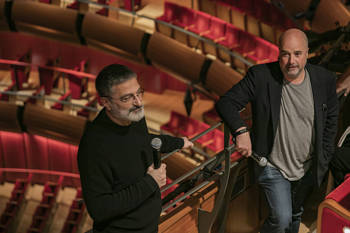Andreas Dracopoulos, President of the Stavros Niarchos Foundation, standing at the Greek National Opera with another man and holding a microphone in their hands